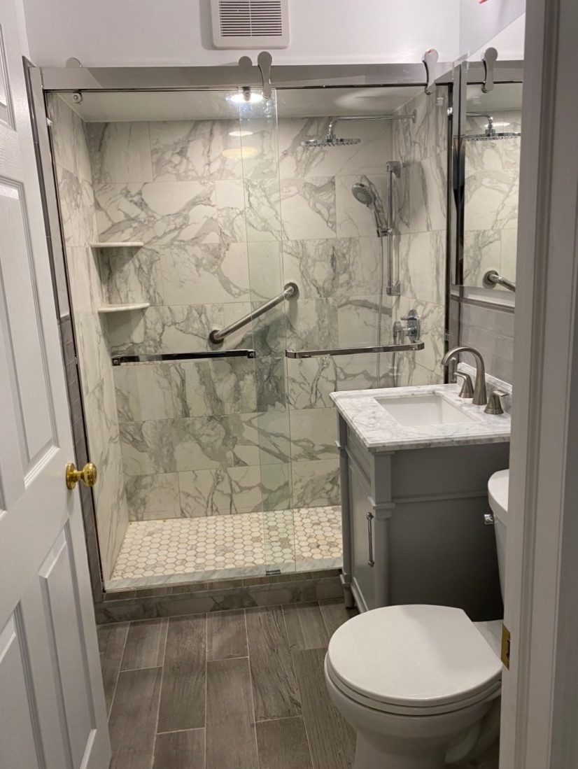 After: marble-look walk-in shower with a grab bar, glass door and new vanity