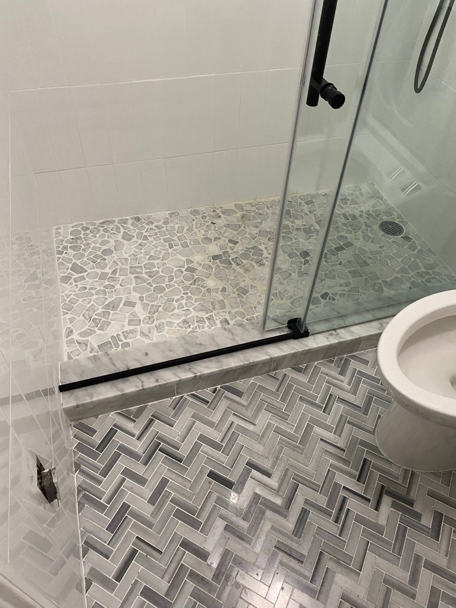 Finished shower with a pebble floor, herringbone tile and glass door